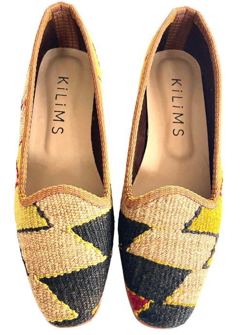 A pair of women's kilim loafers in black, beige, and yellow, featuring a geometric zigzag pattern.