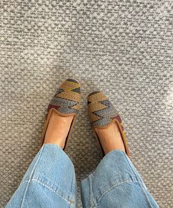 Pair of patterned loafers worn with light blue jeans on a textured gray floor.