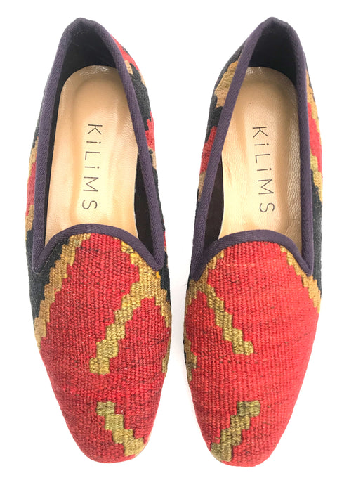 A pair of women's kilim slippers with a colorful red, green, and black geometric pattern, featuring a closed vamp and a slight heel.