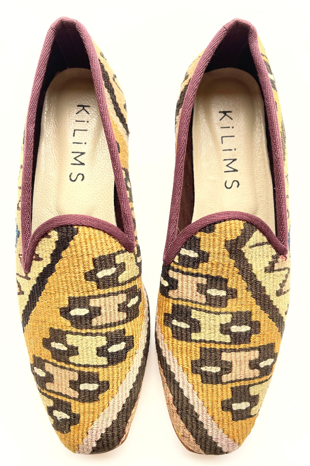 A pair of women's kilim slippers with a geometric pattern in beige, black, and burgundy colors.