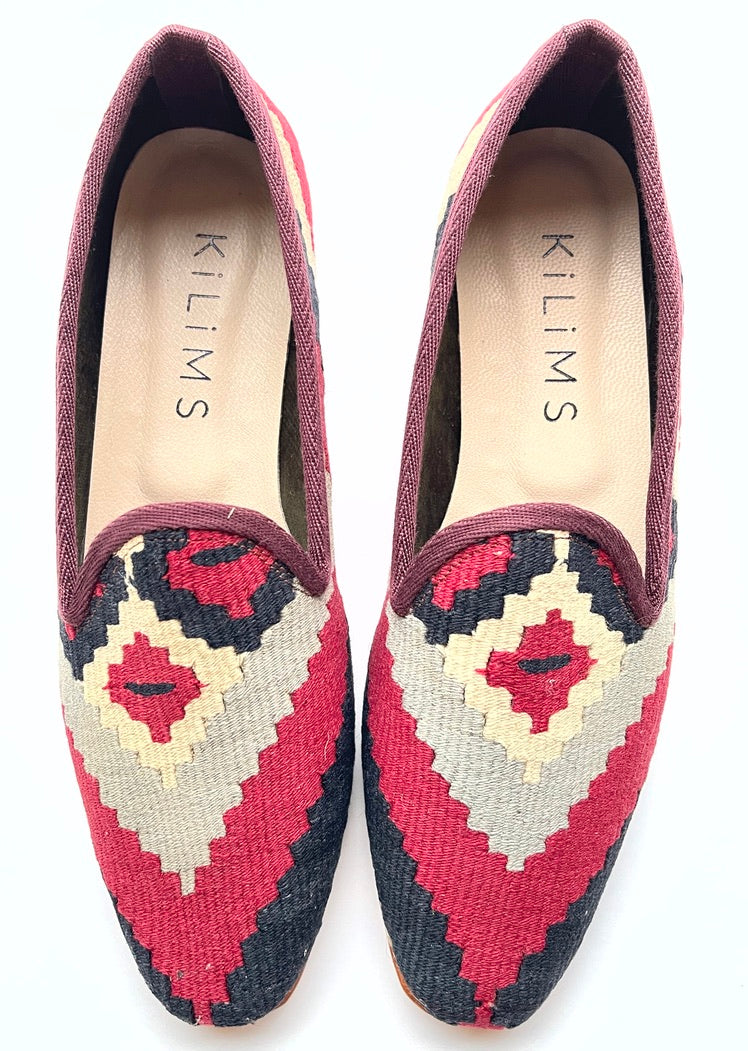 A pair of women's kilim slippers with a burgundy, black, and beige upper and a colorful floral pattern sole.